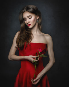 Brunette beautiful woman stands holding a red rose with her eyes closed on a grey background 